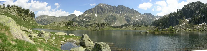 Lago de montaña rodeado de prados y cumbres rocosas